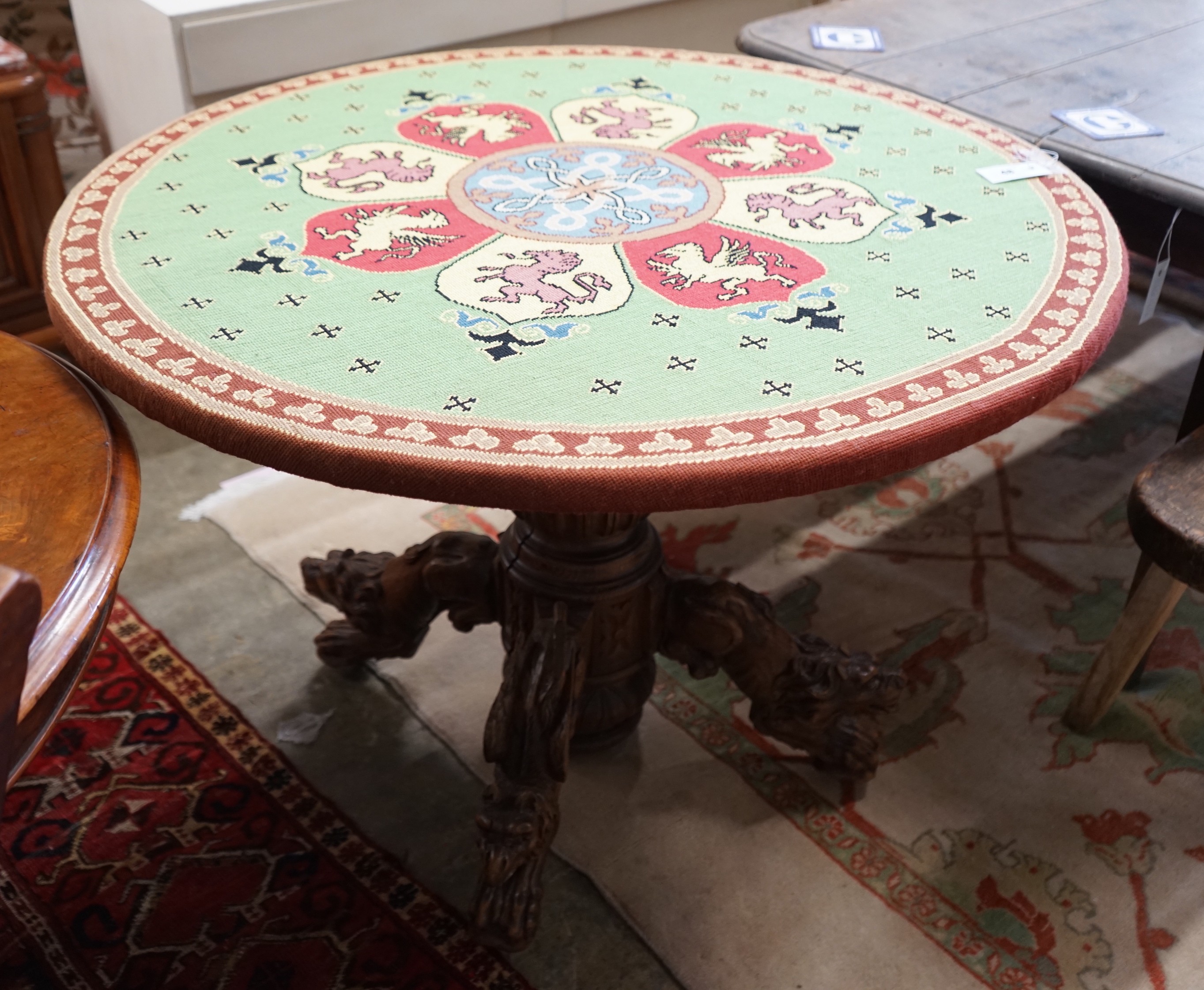 An early 20th century Continental carved oak circular centre table with heraldic tapestry top on winged lion supports, diameter 102cm, height 74cm